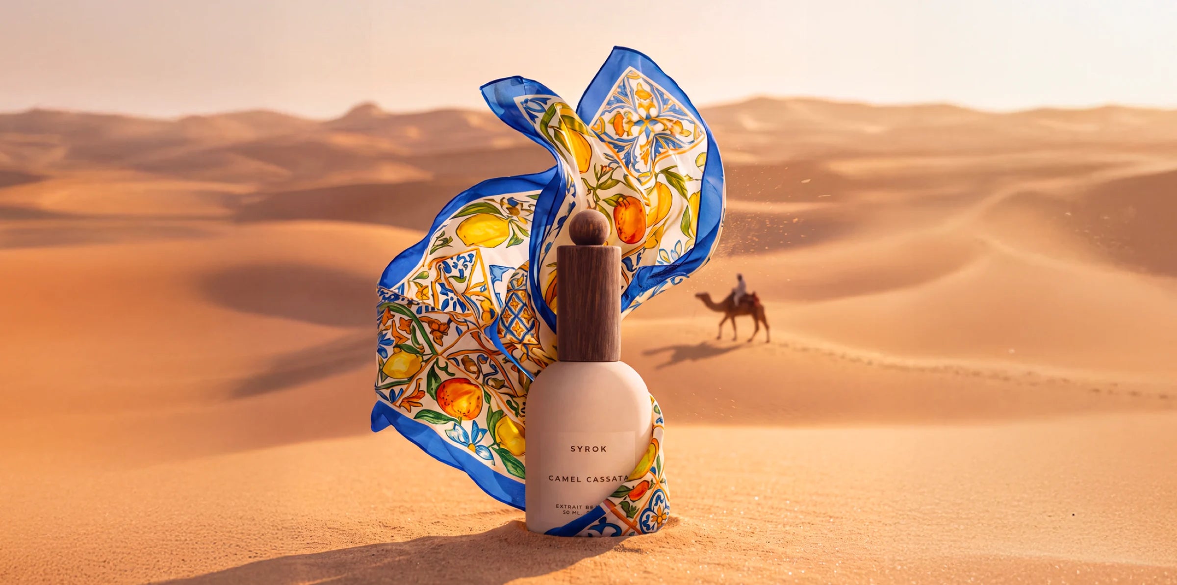 Syrok Camel Cassata bottle among the dunes, with a Sicilian maiolica-patterned scarf